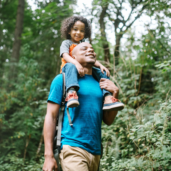 Father Carries Son On Hike Through Forest